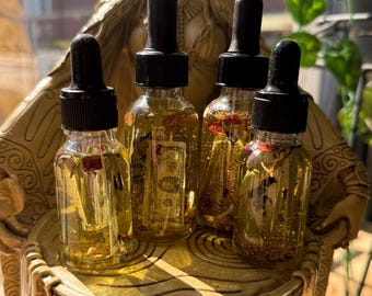 May include: Five small glass bottles with gold glitter and dried flowers inside. The bottles have black dropper tops and are arranged on a gold decorative stand.