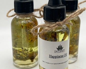 May include: Three glass dropper bottles filled with yellow liquid and botanical elements. Each bottle has a black cap and is tied with twine. The label reads "Happiness Oil" with the text "Use in rituals or on items to increase happiness."