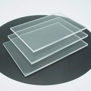 May include: Three clear acrylic sheets stacked on top of each other on a black surface.