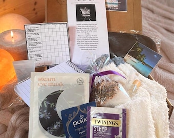 May include: A cardboard box containing a Calm Anxiety Sleep Kit with a printed information sheet, a daily tracking grid, a steam eye mask, a Pukka night tea bag, a Twinings Sleep tea bag, a small black stone, a small vial, and white fuzzy socks.
