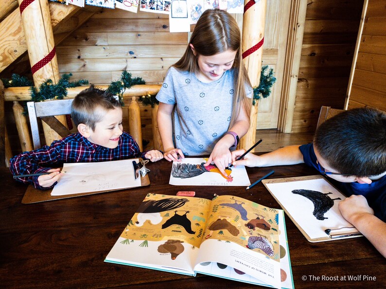 May include: Three children are sitting at a wooden table, drawing and coloring in a book about chickens. The book is open to a page with illustrations of different types of chickens. The children are using pencils and crayons to color the pictures.