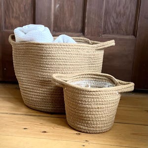 May include: Two brown rope storage baskets, one larger than the other, with a white towel in the larger basket.