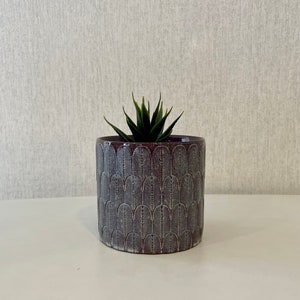 May include: A dark grey ceramic planter with a white geometric pattern. The planter has a small succulent plant inside.