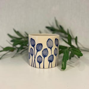 May include: A white ceramic mug with a blue floral pattern. The mug has a simple, modern design and is perfect for everyday use.