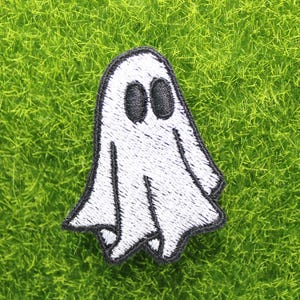 May include: White ghost with black eyes, embroidered patch on a green background.
