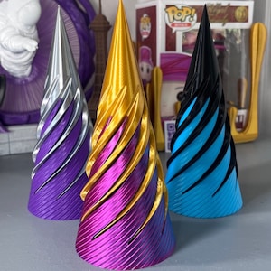 以下が含まれることがあります： スパイラルデザインの装飾的な円錐形のオブジェクトが3つ。1つはシルバーとパープル、もう1つはゴールドとマゼンタ、3つ目は黒と青です。オブジェクトは、テクスチャ加工されたリブ付きの表面と尖った上部を持っています。