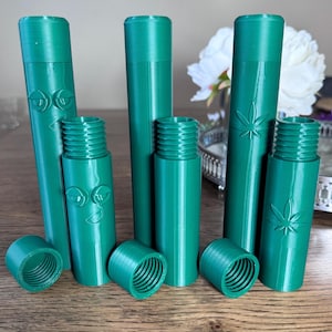 May include: Set of six green plastic containers with different designs. The containers are cylindrical and have a screw-on lid. Some of the containers have a face design, while others have a leaf design.
