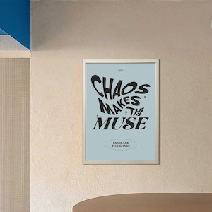以下が含まれることがあります： 青い背景と白いフレームの額縁に入ったポスター。ポスターには、「Chaos Makes The Muse」という黒い文字が書かれており、その下に「Embrace The Chaos」という文字が小さなフォントで書かれている。ポスターは、丸い天板と3本の脚を持つ木製のテーブルの上にある薄いベージュの壁にかけられている。