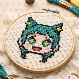 May include: A cross-stitch project in a wooden embroidery hoop featuring a pixelated anime-style character head with teal hair, yellow star-shaped eyes, and pink accents. The design is stitched on white Aida fabric, accompanied by embroidery floss.