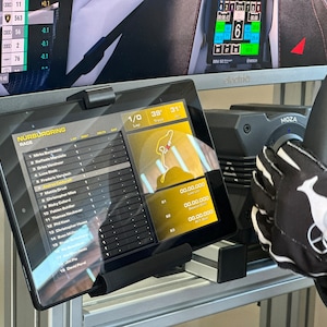 May include: A black tablet displaying a racing leaderboard with the text "N&Uuml;RBURGRING RACE" and a map of the racetrack. The tablet is mounted on a stand and is positioned in front of a computer monitor displaying a racing game.