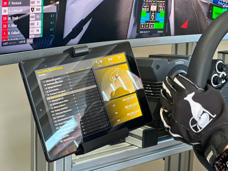 May include: A black tablet displaying a racing leaderboard with the text "N&Uuml;RBURGRING RACE" and a map of the racetrack. The tablet is mounted on a stand and is positioned in front of a computer monitor displaying a racing game.