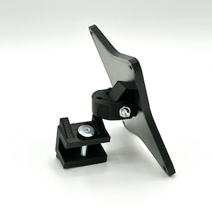 May include: Black plastic phone mount with a swivel joint and a clamp. The mount is designed to attach to a desk or other surface.