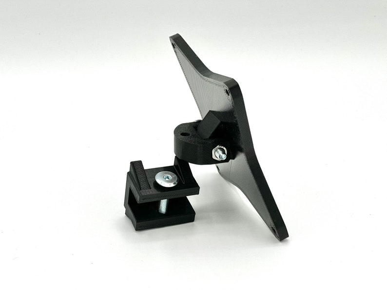 May include: Black plastic phone mount with a swivel joint and a clamp. The mount is designed to attach to a desk or other surface.