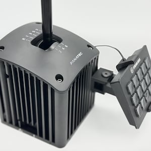 May include: A black Fanatec gear shifter with a vertical stick and a gear pattern diagram printed on the top surface. Attached to the side is a black Stream Deck control panel featuring a grid of twelve square buttons connected by a thin cable.