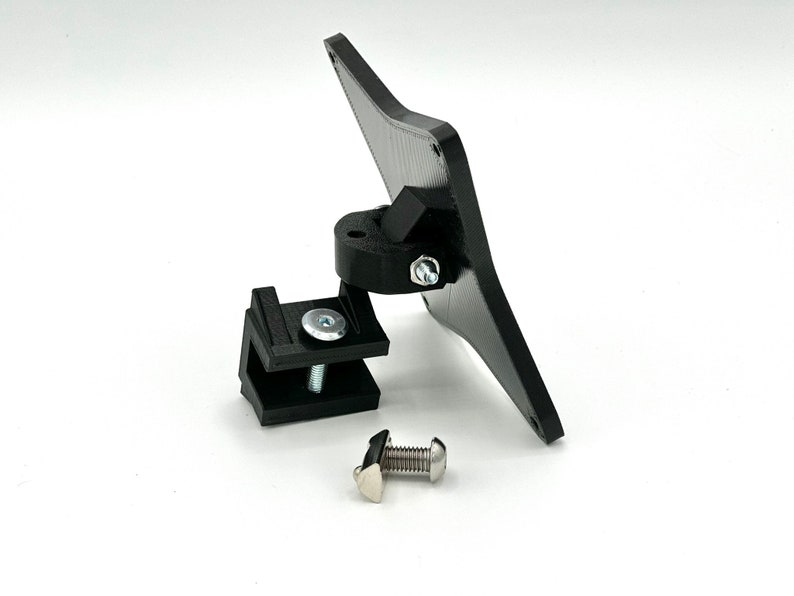 May include: A black plastic mount with a swivel joint and a clamp. The mount is designed to attach to a surface and hold a device, such as a camera or a phone.