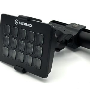 May include: Black Stream Deck with 15 illuminated buttons, mounted on a black adjustable arm. The Stream Deck has the Stream Deck logo in white. The buttons are arranged in a 4x4 grid, with one button missing.
