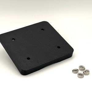 May include: A black plastic square plate with four holes and a raised edge. Four silver metal washers are included.