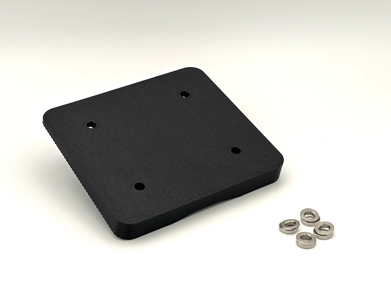 May include: A black plastic square plate with four holes and a raised edge. Four silver metal washers are included.