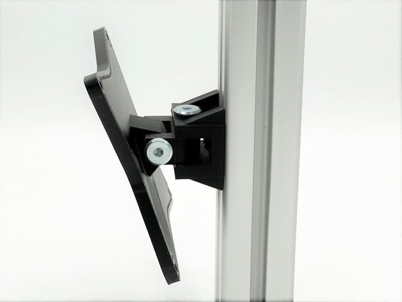 May include: A black plastic bracket with two screws attached to a silver metal pole. The bracket is designed to hold a flat surface, such as a shelf or a sign.