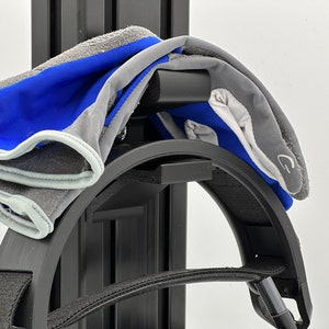 May include: A black headband with a grey and blue pair of gloves hanging on it. The headband is attached to a black metal stand.
