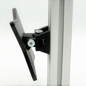 May include: A black plastic bracket with two screws attached to a silver metal pole. The bracket is designed to hold a flat surface, such as a shelf or a sign.