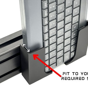 Könnte beinhalten: Ein schwarzer Keyboardhalter aus Kunststoff mit einer grauen Tastatur im Inneren. Der Halter ist so konzipiert, dass er zu einer Tastatur jeder Größe passt. Der Text "FIT TO YOUR REQUIRED SIZE" ist unter dem Halter aufgedruckt.