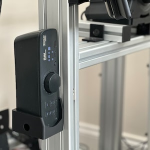 May include: A black audio interface with a volume knob and a digital display. The interface is mounted on a silver metal rack.