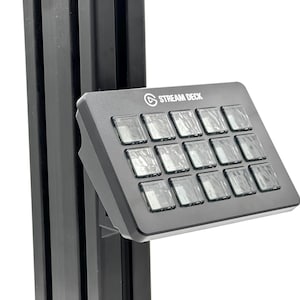 May include: A black Stream Deck with 15 illuminated buttons. The device is mounted on a black support structure. The Stream Deck logo is visible on the top left corner of the device.