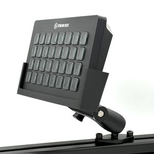 Op de afbeelding: Een zwart Stream Deck met meerdere knoppen, gemonteerd op een zwarte standaard. Het Stream Deck heeft de merknaam afgedrukt in de linkerbovenhoek. De standaard is bevestigd aan een zwarte rail.