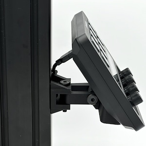 May include: A black device with a screen and buttons mounted on a black pole with a bracket. The device has three knobs on the right side.