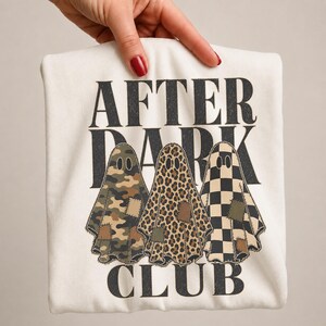 May include: A white t-shirt featuring the black text AFTER DARK CLUB and three ghost illustrations. The ghosts have different patterns: one with green and brown camouflage, one with a brown leopard print, and one with a black and white checkerboard.