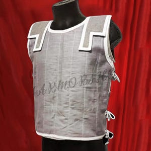 May include: A white sleeveless vest with a padded front and white straps. The vest has a white trim around the edges and is made of a quilted material.