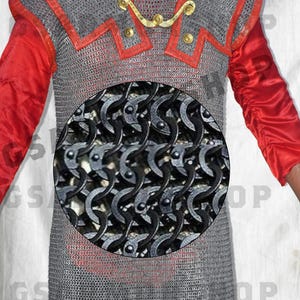 May include: A silver chainmail shirt with red trim. The chainmail is made of interlocking metal rings. The shirt is worn by a person with a red shirt underneath.