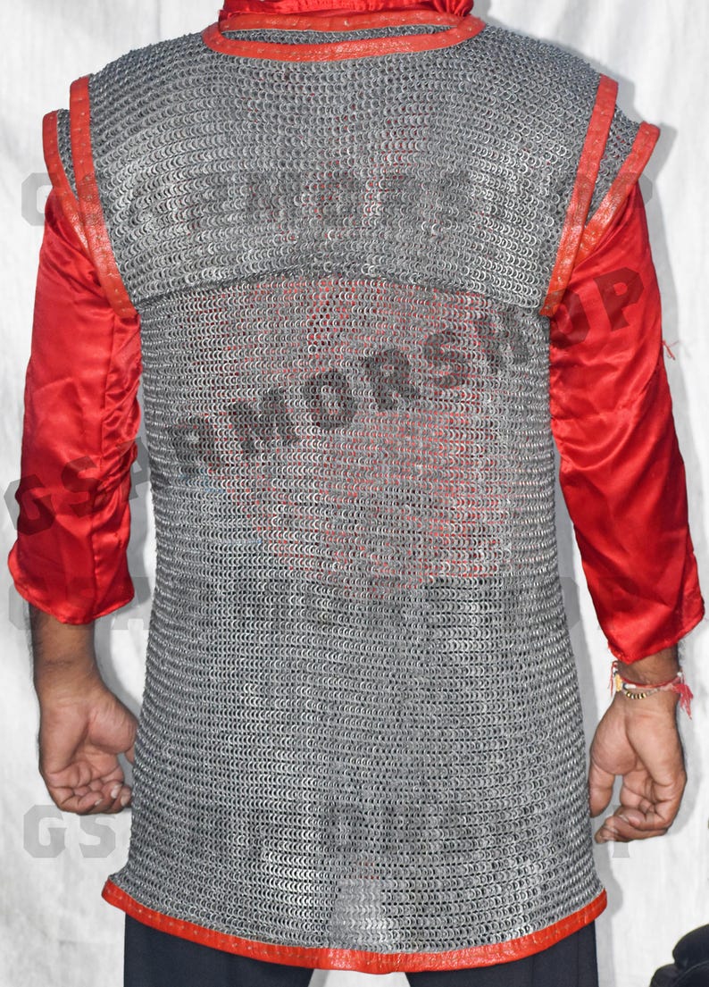May include: A silver chainmail shirt with red leather trim. The shirt is being worn by a person, but their face is not visible. The shirt is made of interlocking metal rings.