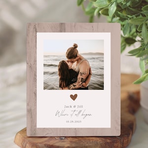 May include: A wooden photo frame with a picture of a couple kissing on a beach. The frame has a light brown color and includes the text "Jack & Jill Where it all began 10.28.2023" with a heart symbol.