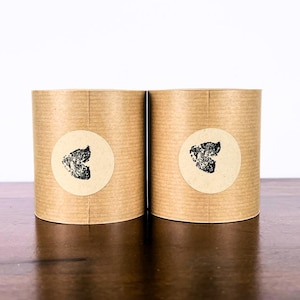 May include: Two brown paper tubes with black and white butterfly stickers. The stickers are round and feature a black butterfly design on a white background.