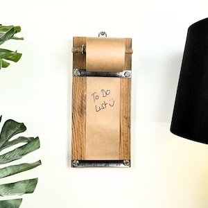 May include: A wooden wall mounted to-do list holder with a roll of brown paper and a metal ruler. The paper has the words "To Do List" written on it.