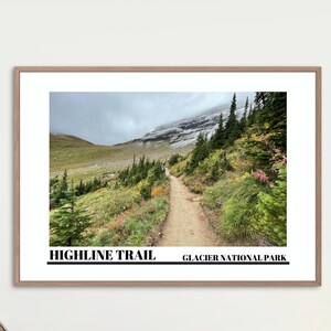 May include: A framed print of a hiking trail in Glacier National Park. The trail is a dirt path winding through a forest of trees and green foliage. The text "HIGHLINE TRAIL GLACIER NATIONAL PARK" is printed at the bottom of the print.