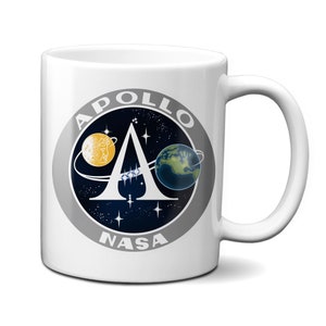Könnte beinhalten: Weiße Keramiktasse mit einem schwarz-weißen NASA Apollo-Missionslogo mit den Buchstaben "APOLLO" und "NASA" und einem stilisierten Buchstaben "A" mit einer Darstellung der Erde und des Mondes im Hintergrund.