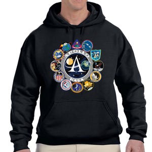 Peut inclure: Sweat-shirt à capuche noir avec un imprimé graphique des missions Apollo. Le graphique présente un cercle de logos avec le texte "Apollo NASA" au centre.