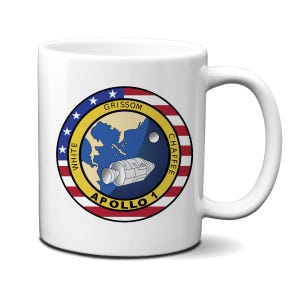 May include: White ceramic mug with a colorful Apollo 1 mission patch featuring the names "Grissom", "White", and "Chaffee" around a depiction of the Apollo 1 spacecraft.