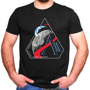 Peut inclure: T-shirt noir avec un graphique en triangle blanc représentant une lune croissante, une ligne rouge et bleue, et le texte "Wiseman Glover Koch Hansen".