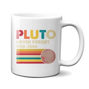 Peut inclure: Une tasse en céramique blanche avec un design rétro coloré comportant le texte "PLUTO NEVER FORGET 1930-2006" et une image stylisée de Pluton.