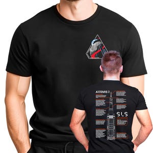 Puede incluir: Camiseta negra con un pequeño gráfico triangular en la parte delantera, que representa una luna y un cohete. La parte trasera de la camiseta muestra un diagrama de un cohete con el texto "ARTEMIS 2" y "SLS SPACE LAUNCH SYSTEM".