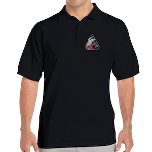May include: Black polo shirt with a small embroidered patch on the left chest. The patch is a triangle with a red, white, and blue design.