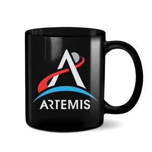May include: Black ceramic mug with a white NASA Artemis logo featuring a stylized letter A with a red and blue orbit around it. The text "ARTEMIS" is printed below the logo.