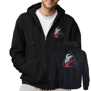 Może przedstawiać: Czarna bluza z kapturem zapinana na zamek z białym t-shirtem pod spodem. Bluza ma trójkątną grafikę z planetą, czerwonymi liniami i literą "A". Poniżej pokazano pasującą kurtkę.