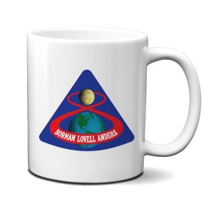 Könnte beinhalten: Weiße Keramik-Kaffeetasse mit einer blauen und roten Grafik der Erde, des Mondes und einer roten Umlaufbahn um sie herum. Der Text "Borman Lovell Anders" ist unter der Grafik gedruckt.