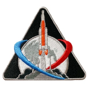 May include: A black triangular patch with a white moon and a rocket launching from it. The rocket is orange and white with flames. A blue and red crescent shape surrounds the moon.