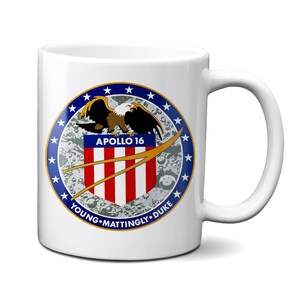 Puede incluir: Taza de cerámica blanca con un parche de la misión Apolo 16 de colores. El parche muestra una bandera estadounidense, un águila y el texto "Apolo 16, Young, Mattingly, Duke".